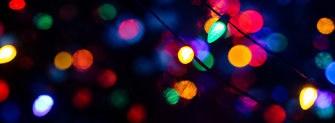 A blurry close-up of various Christmas lights in the dark, with a faceted green C9 bulb in clear focus.