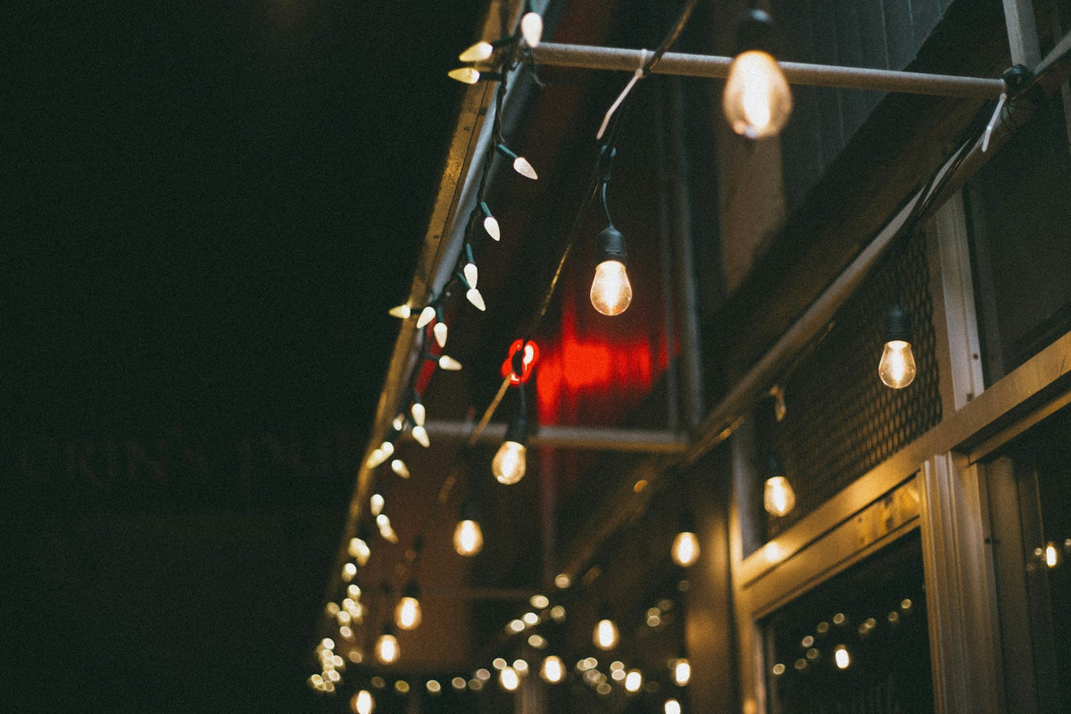 The underside of a patio overhang, in which white faceted Christmas light bulbs and white globe lights are shining together at night.